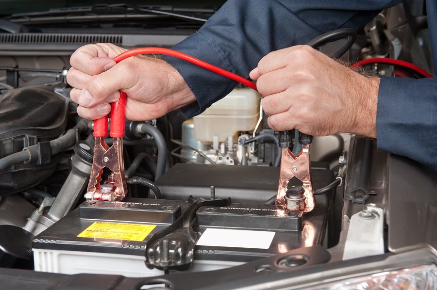 Battery Jumpstart - a man holding jumper cables on a car battery.